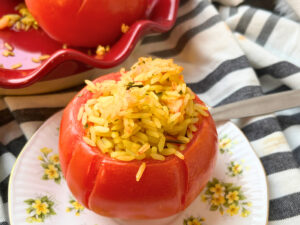 A stuffed tomato on a yellow floral plate. There are more tomatoes in the background.