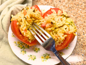 A yellow floral plate with a stuffed tomato. The tomato is cut in half and there is a fork resting on it.