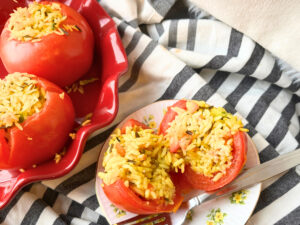 A dish of stuffed tomatoes with rice. There is one tomato in a yellow floral plate. This tomato is cut in half.