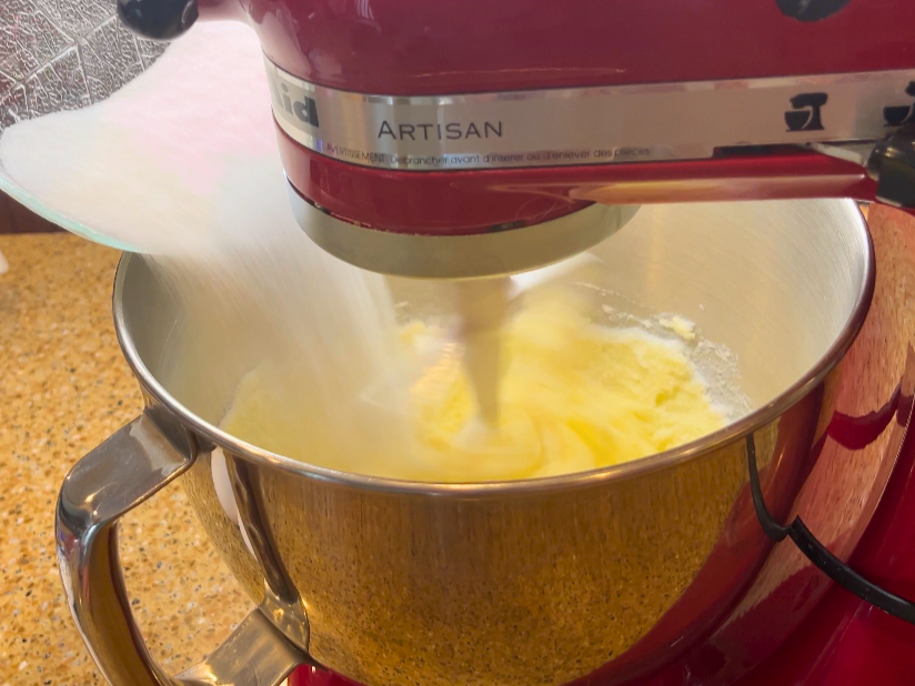 Woman adding sugar to a stand mixer with butter inside.