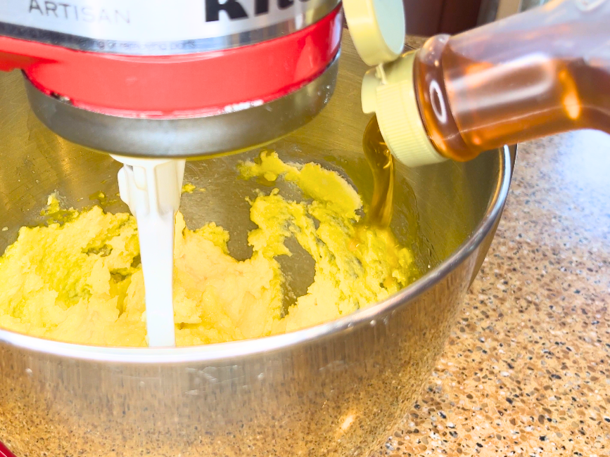 A woman adding corn syrup to a stand mixer.
