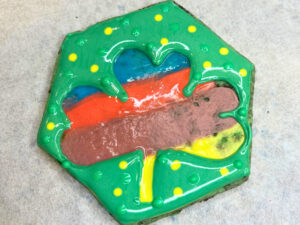 A green decorated sugar cookie with a rainbow background in the shape of a clover.