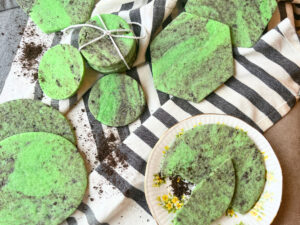 Green and black marbled sugar cookies on a grey and white cloth. One of the cookies is on a yellow floral plate.