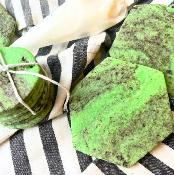 Green and black marbled sugar cookies on a grey and white cloth. There is a icing bag in the background.