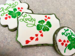 A group of 3 sugar cookies decorated with royal icing. They have clover and hearts on them.