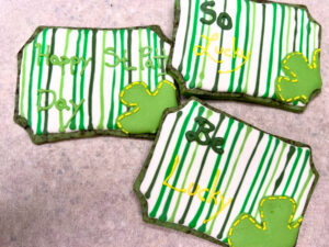 A group of three sugar cookies decorated with royal icing. They have a clover design and have words piped on them.
