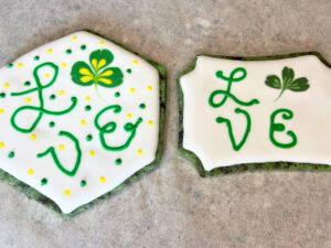 Two sugar cookies decorated with royal icing they have lettering and a clover on them.