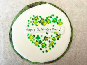 A green sugar cookie decorated with royal icing. It has a clover design and says Happy St. Patrick's Day on it.