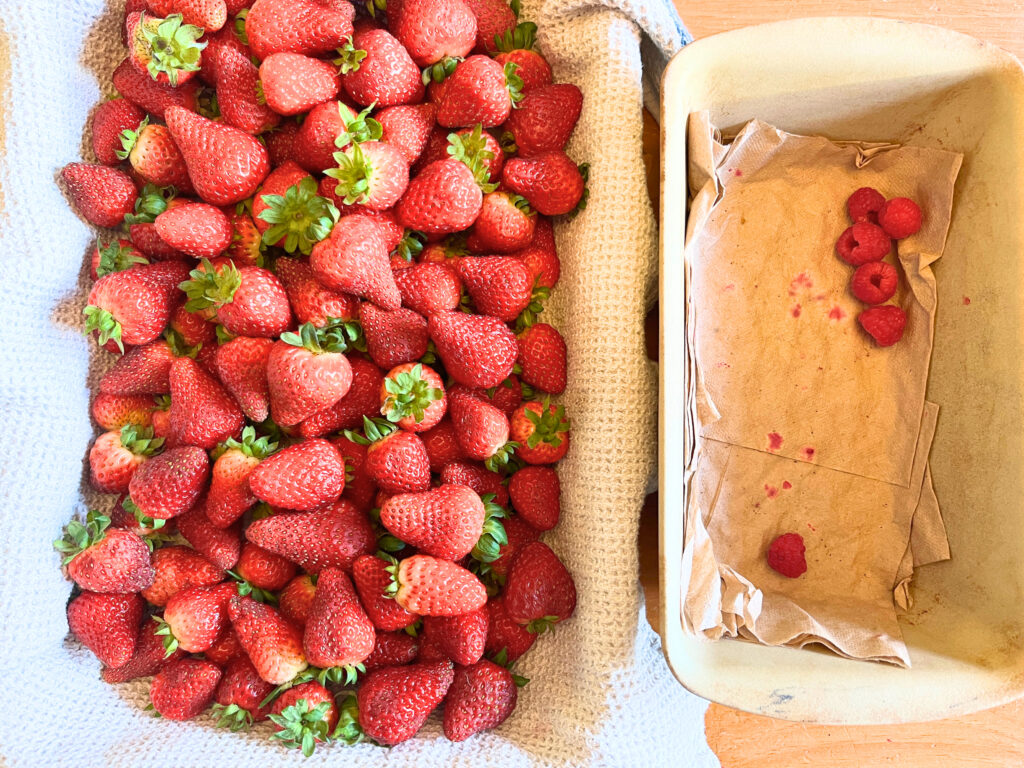 A casserole dish with fresh strawberries. A loaf pan with raspberries inside.