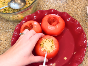 A woman stuffing tomatoes with rice, using a spoon.