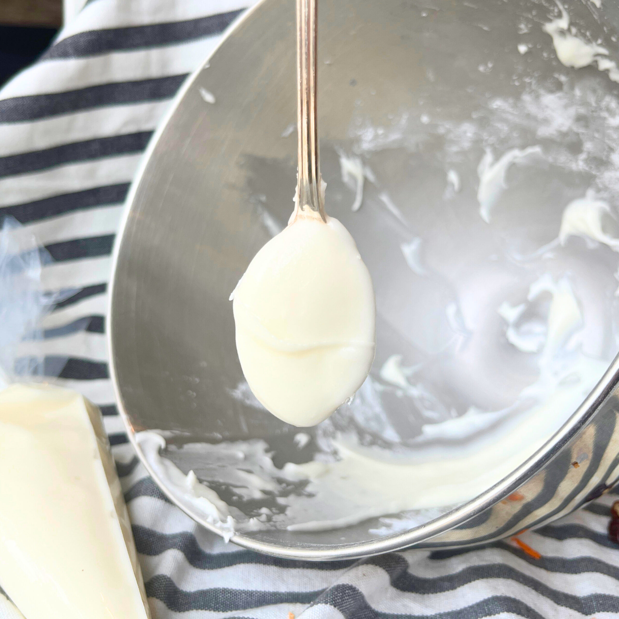 A mixing bowl with white icing inside. A piping bag with white icing inside and a spoon with white icing in the scoop.
