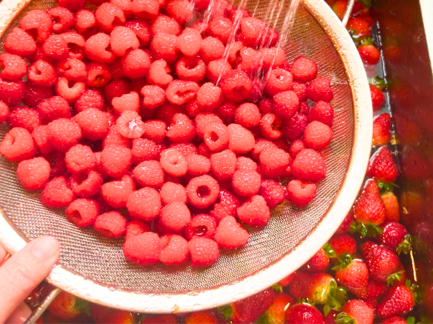 A woman rinsing a colander full of raspberries.