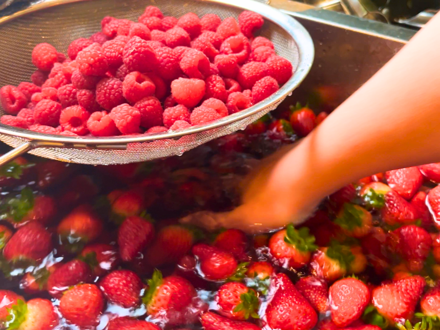 A woman mixing strawberries in a sink full of water.