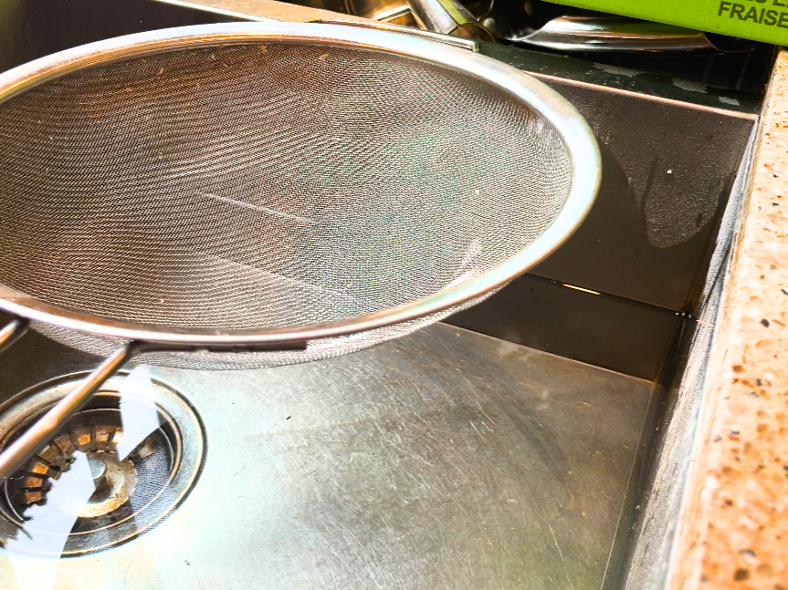 A sink full of water with a colander resting on top 