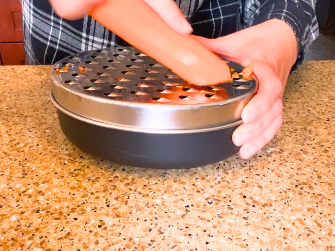 A woman grating a carrot using a cheese grater.