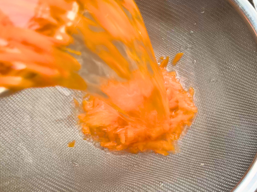Pouring shredded carrots and water through a colander.
