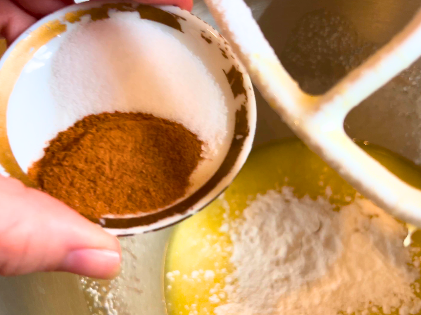 Woman adding salt and cinnamon to the bowl of a stand mixer.