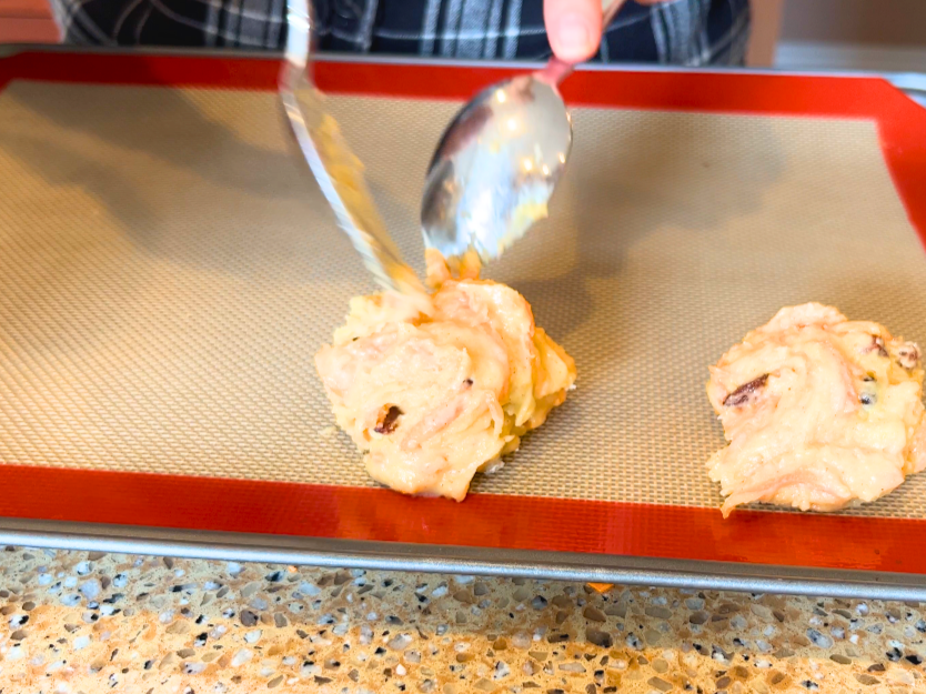 A woman spooning cookie dough onto a lined baking sheet.