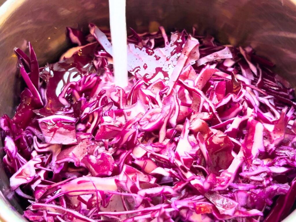 A pot with shredded red cabbage inside. There is water being added to the pot.