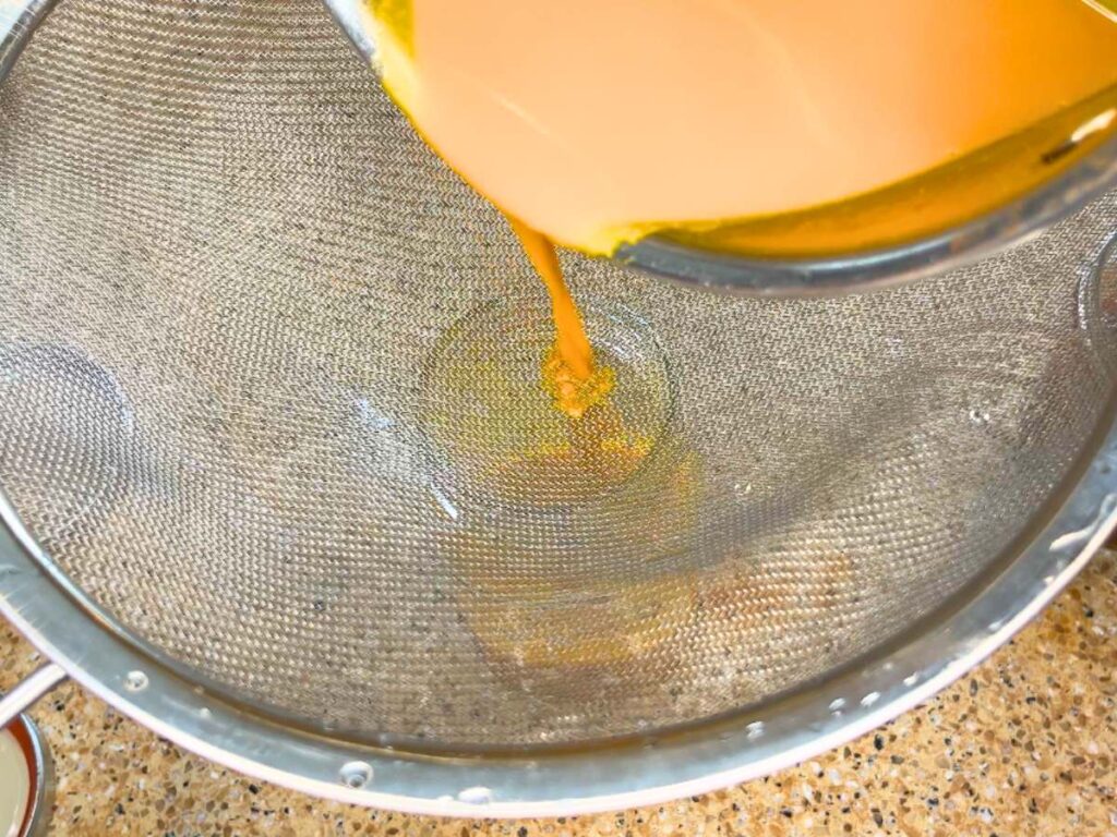 A woman pouring a yellow liquid through a strainer.