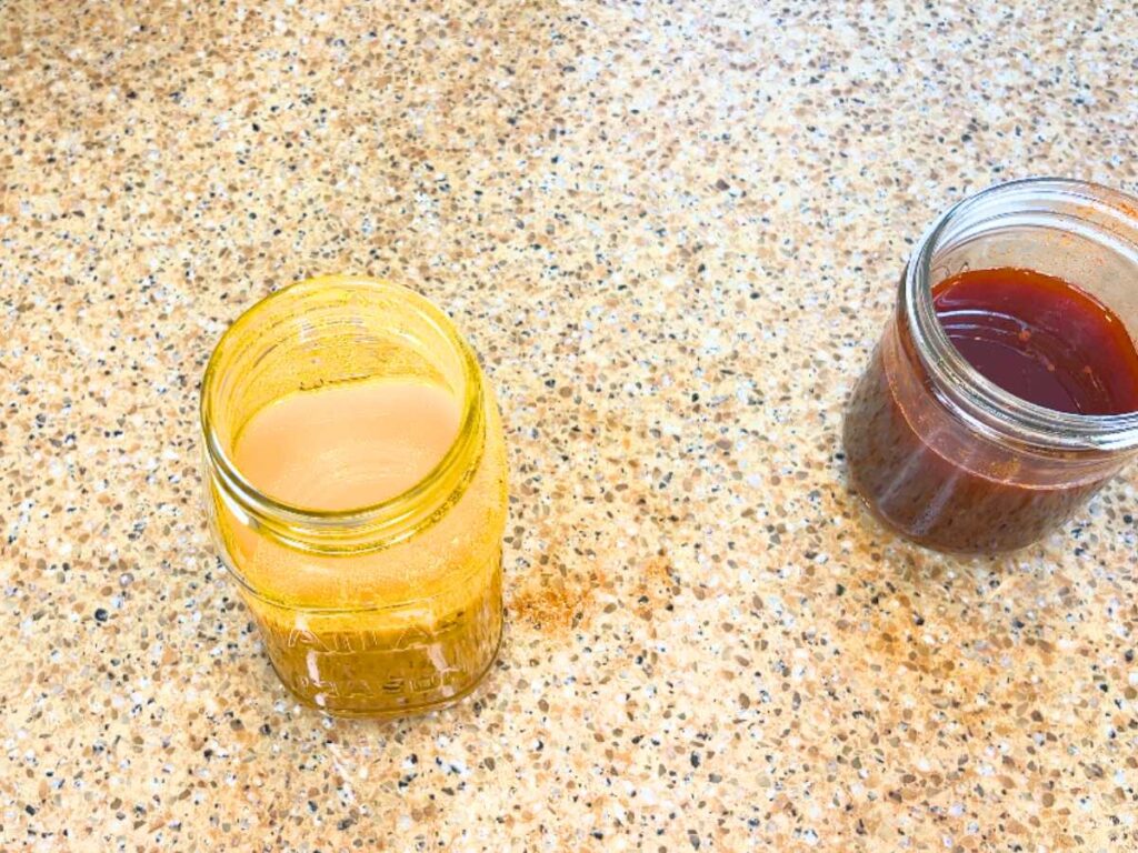 Two canning jars on a counter top. One has yellow liquid and one has a reddish-brown.