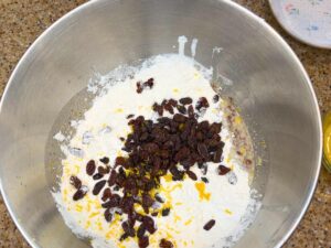 A mixing bowl with flour, raisins, and lemon zest inside.