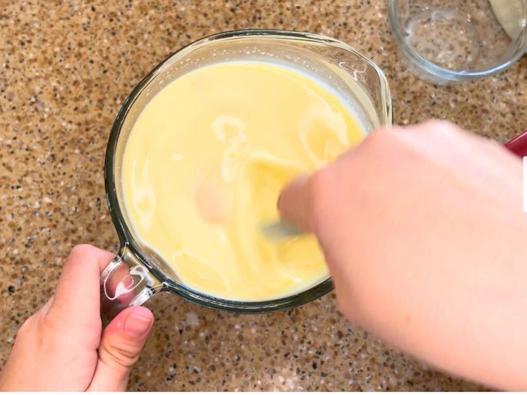 Woman stirring a light yellow liquid inside of a glass measuring cup.