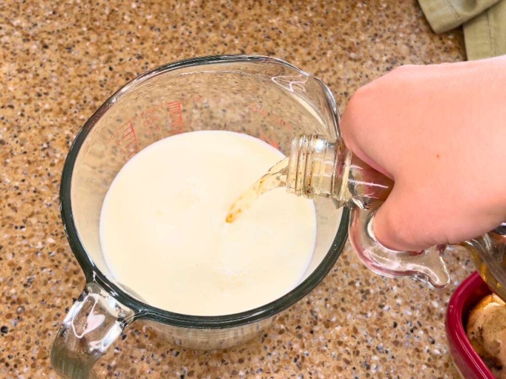 Woman pouring vanilla into a glass measuring cup with milk inside.