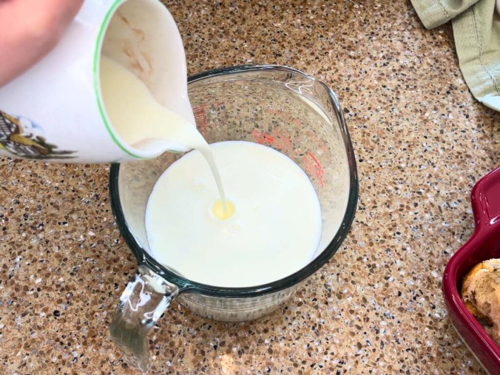 Woman pouring cream into a glass measuring cup with milk inside.