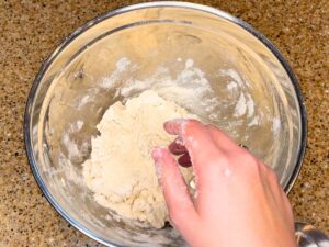 Woman mixing dough in a bowl with her hands.