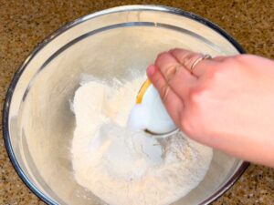 A woman pouring salt into a bowl of flour.