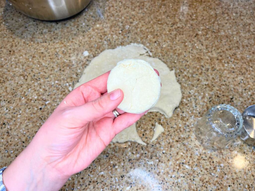 A woman holding a circle of dough. There is more dough in the background.