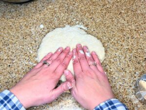 A woman patting out some dough with her hands.
