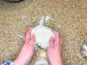 A woman holding a ball of dough on a counter top.