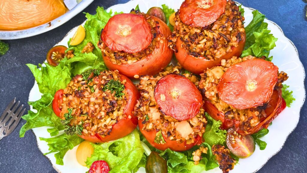 A plate of stuffed tomatoes with rice on a bed on lettuce.
