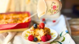 A woman is pouring syrup onto a plate of breakfast casserole with berries on top.