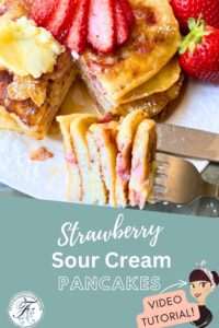 A pinterest pin for strawberry sour cream pancakes. In the picture there is a stack of pancakes with strawberries on the plate. There is a fork full of a slice with layers of pancakes.