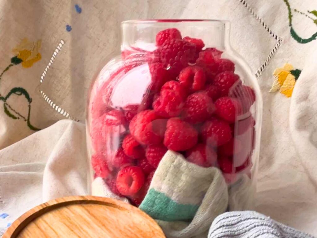 A glass jar filled with raspberries.