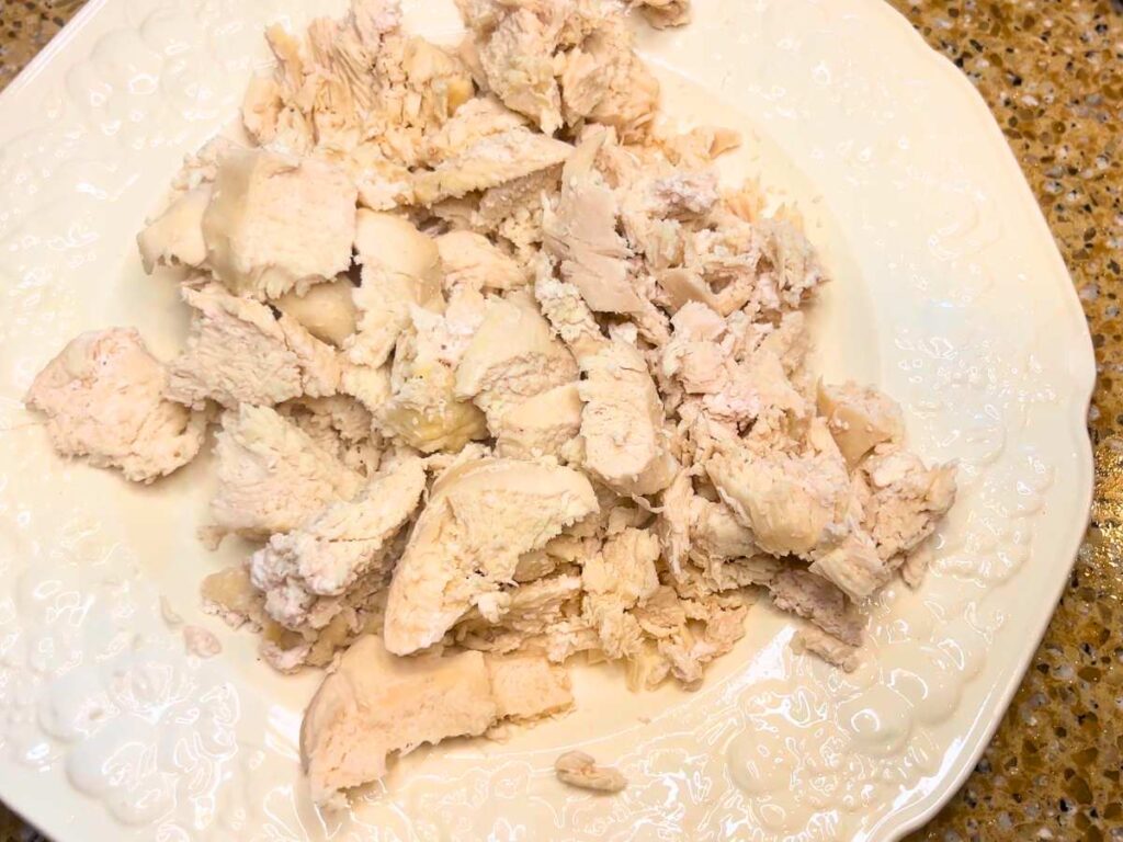A white floral plate with shredded cooked chicken.