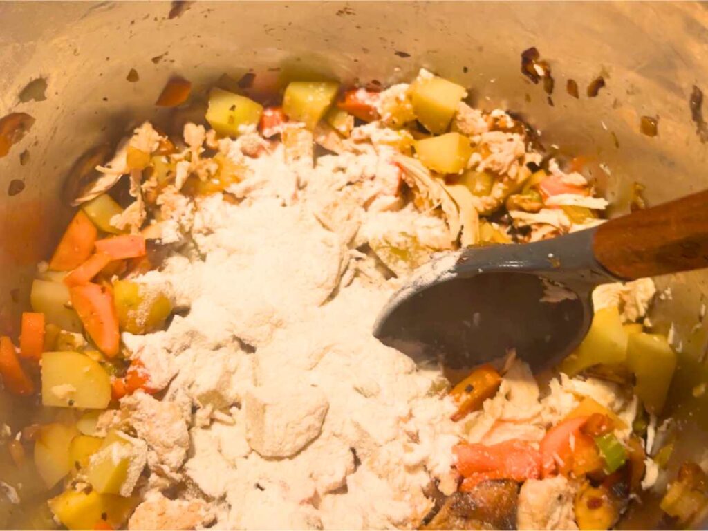 A chicken and vegetable mixture in a large metal pot. There is flour sprinkled on top.