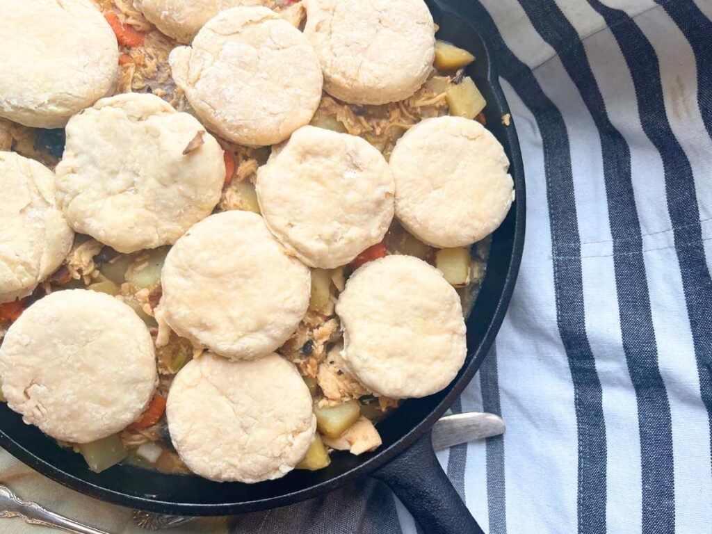 A cast iron skillet with a cooked mixture of chicken and vegetables in side. There are unbaked disks of dough on top.
