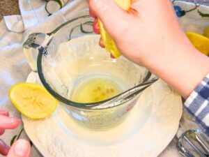 A woman squeezing lemons into a glass measuring cup.