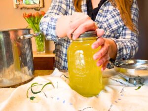 A woman screwing a lid onto a glass canning jar. The jar has yellow liquid inside.