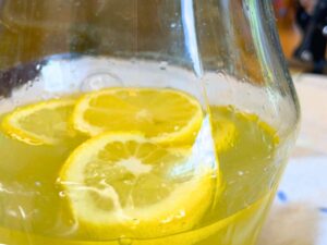 A yellow liquid in the bottom of a glass pitcher. There are slices of lemon inside.