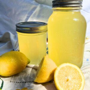 Two canning jars with yellow liquid inside. There are lemons in the foreground.