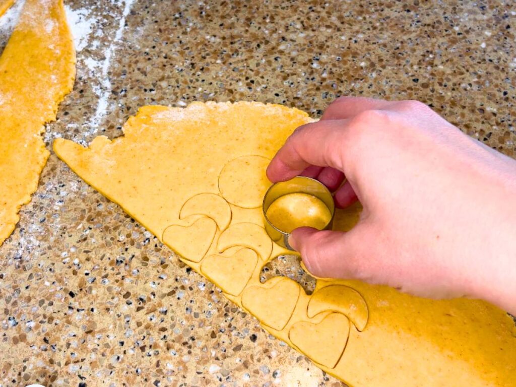 A woman using a small circle cookie cutter to cut out dough
