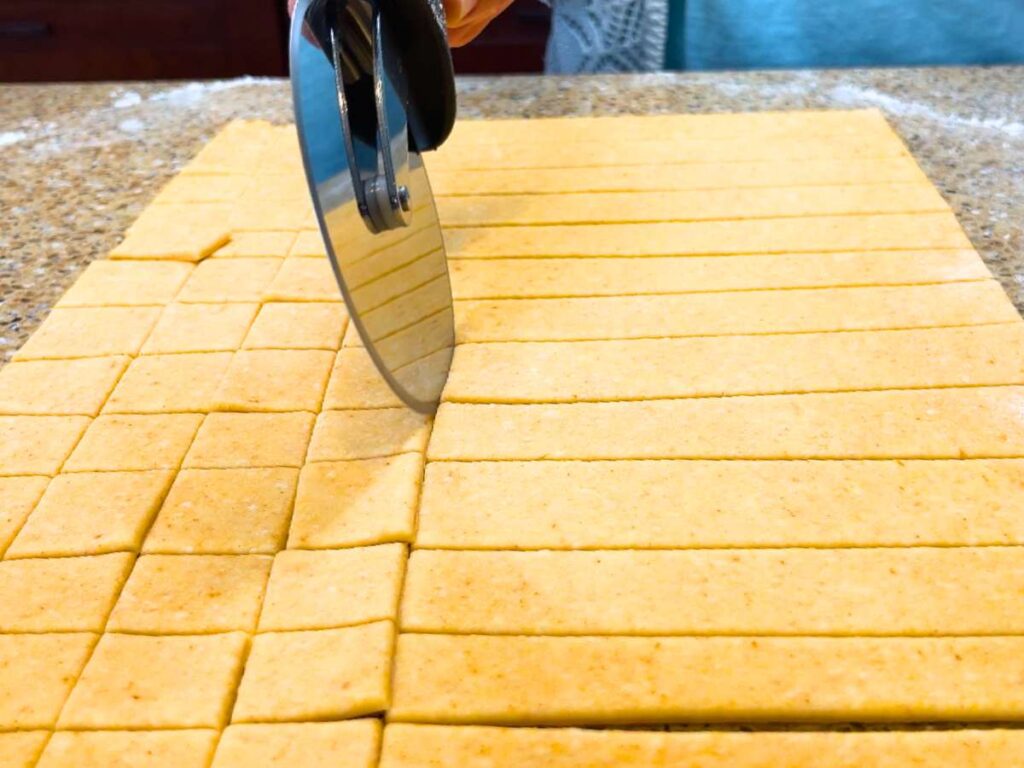 A woman using a pizza wheel to cut dough into squares