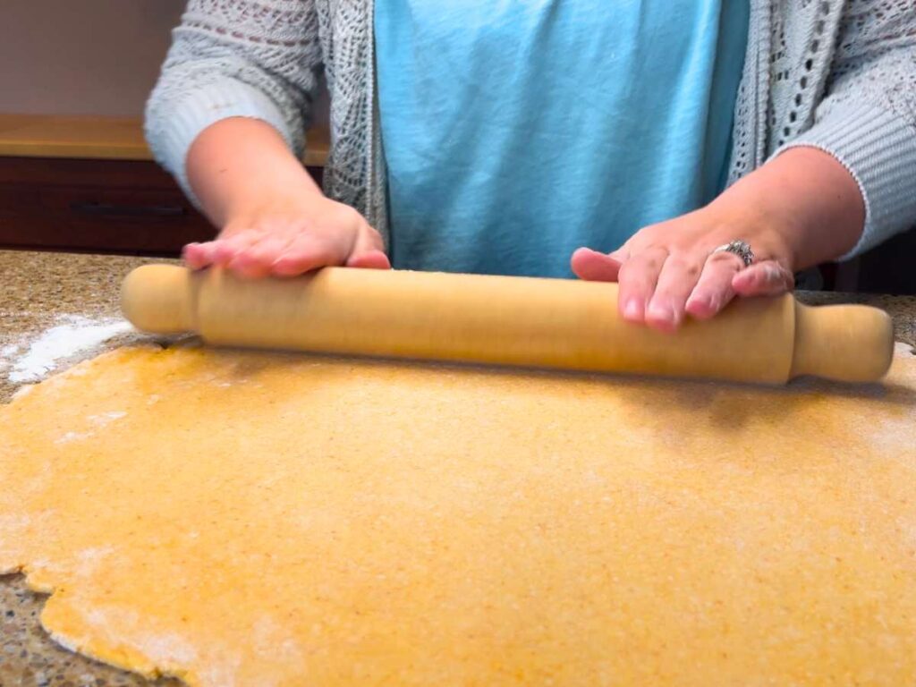 A woman using a wooden rolling pin to roll out a large sheet of dough