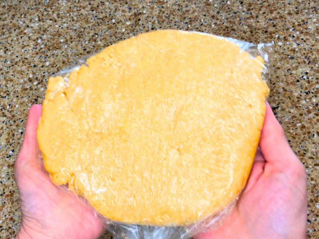 An orange dough wrapped in plastic wrap. A woman is holing it in her hands