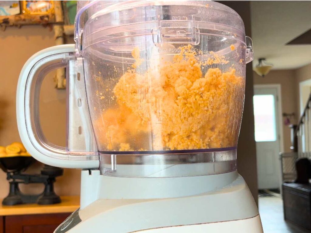 A clumped orange dough ball in a food processor